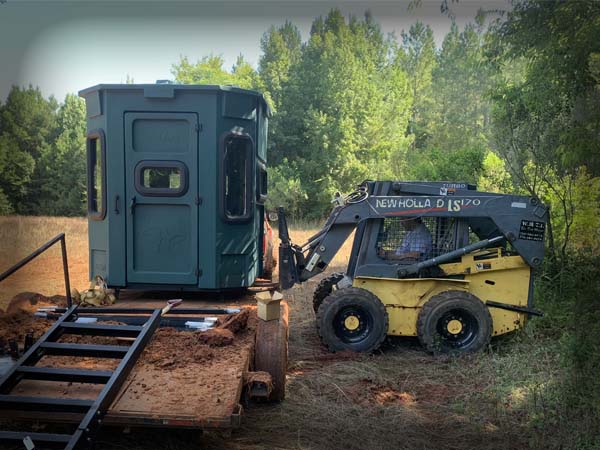 Skid steer unloading a premium hunting blind stand on a trailer
